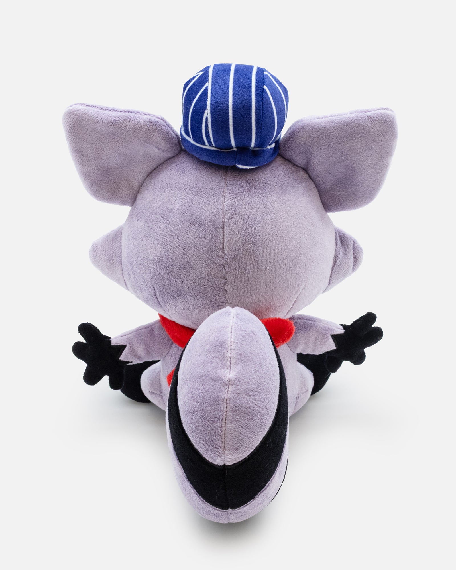 Purple plush toy with a blue cap and red scarf facing back on a white background